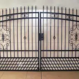 Dwuskrzydłowa, czarna brama ogrodzeniowa z metalowymi prętami i ozdobnymi elementami, widoczna od frontu, na jasnym tle.